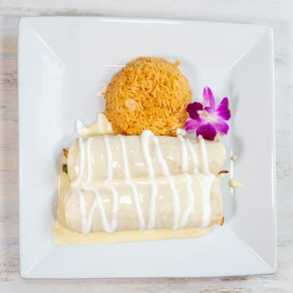 Two enchiladas topped with white sauce, a side of rice, and a purple orchid garnish.