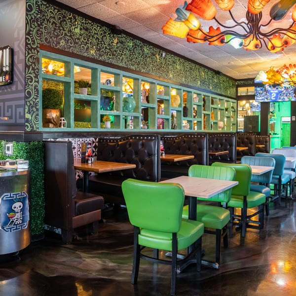 Colorful restaurant interior with green and blue chairs, dark booths, and decorative shelves under unique chandeliers.
