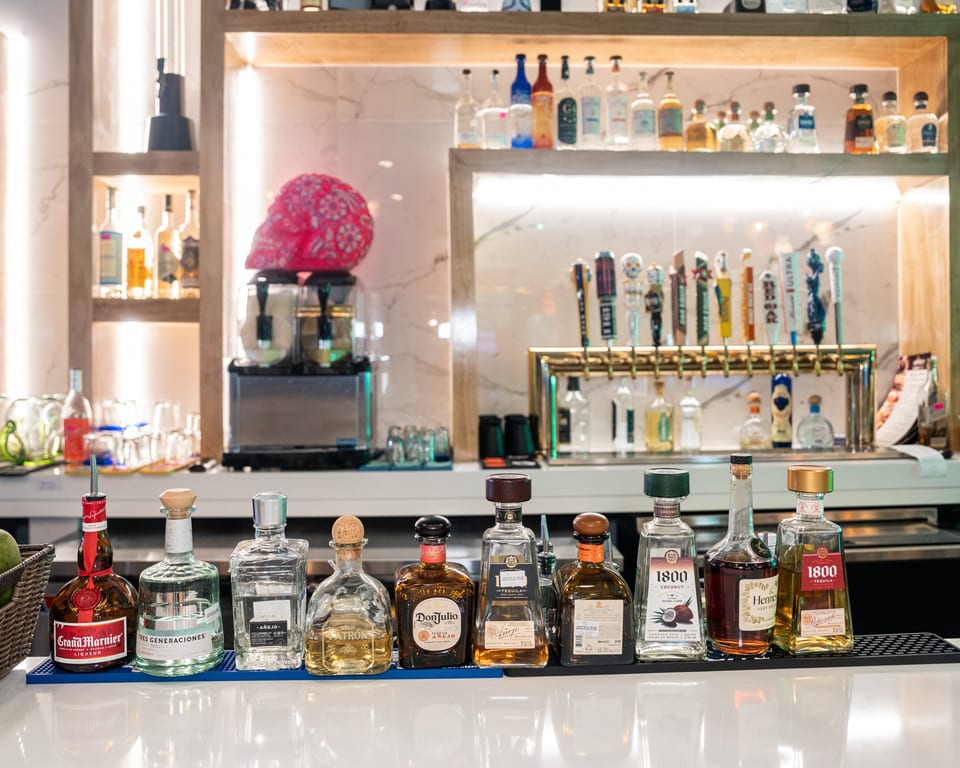 A bar counter displays a variety of tequila bottles, with beer taps and liquor shelves in the background.