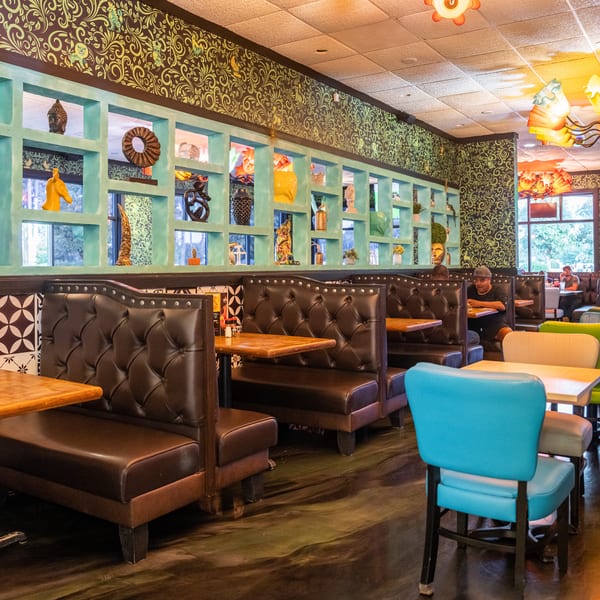 Restaurant interior with brown booths, colorful chairs, decorative wall shelves, and patterned wallpaper.