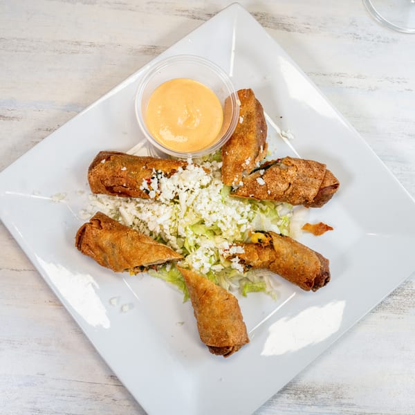 Crispy fried taquitos on a bed of lettuce with crumbled cheese and a side of dipping sauce.