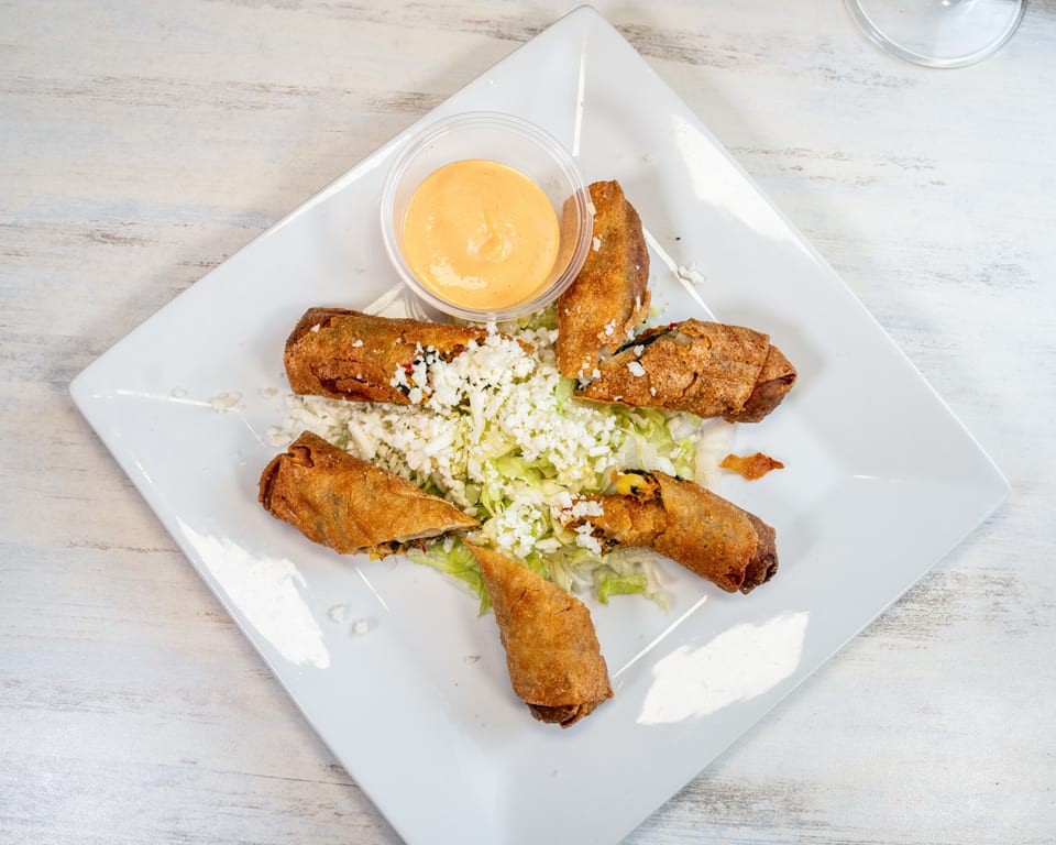 Crispy fried taquitos on a bed of lettuce with crumbled cheese and a side of dipping sauce.