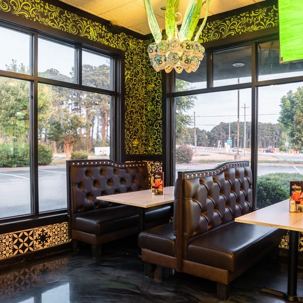 Restaurant interior with dark leather booths, light wooden tables, and large windows overlooking a parking lot.