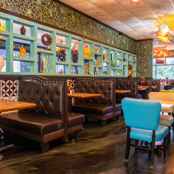 Restaurant interior with brown booths, colorful chairs, decorative wall shelving, and patterned wallpaper.