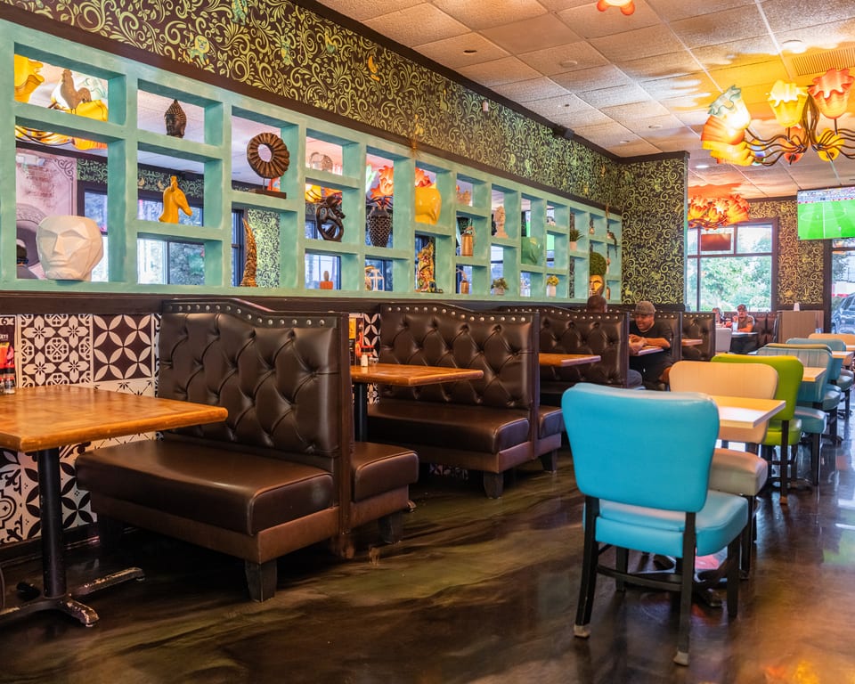 Restaurant interior with brown booths, colorful chairs, decorative wall shelving, and patterned wallpaper.