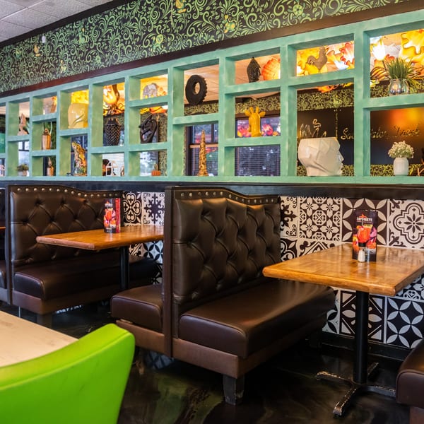 Restaurant interior with dark brown booths, wooden tables, and a decorative wall with green shelves and patterned wallpaper.