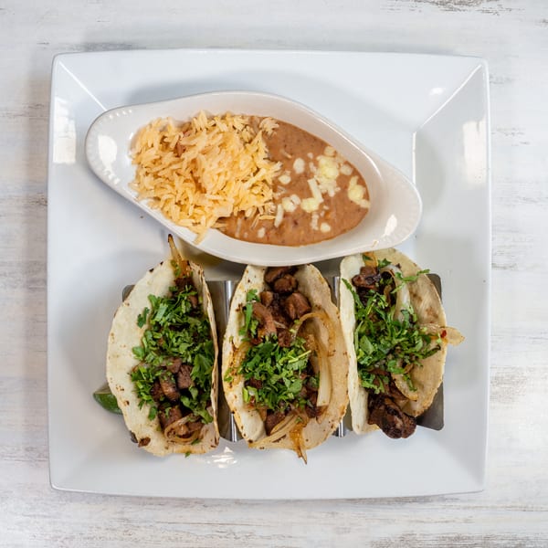 Three street tacos with meat, onions, and cilantro, served with rice and refried beans.