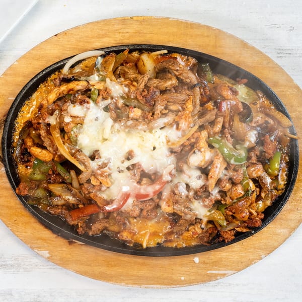 Sizzling fajitas with melted cheese, chicken, beef, peppers, and onions on a wooden platter.
